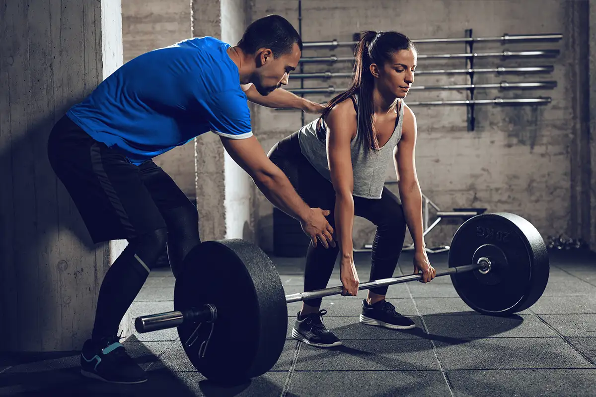 Personal trainer at the gym spotting his client with free weights, showing proper lifting techniques - Collinsville Illinois - Bethalto Illinois